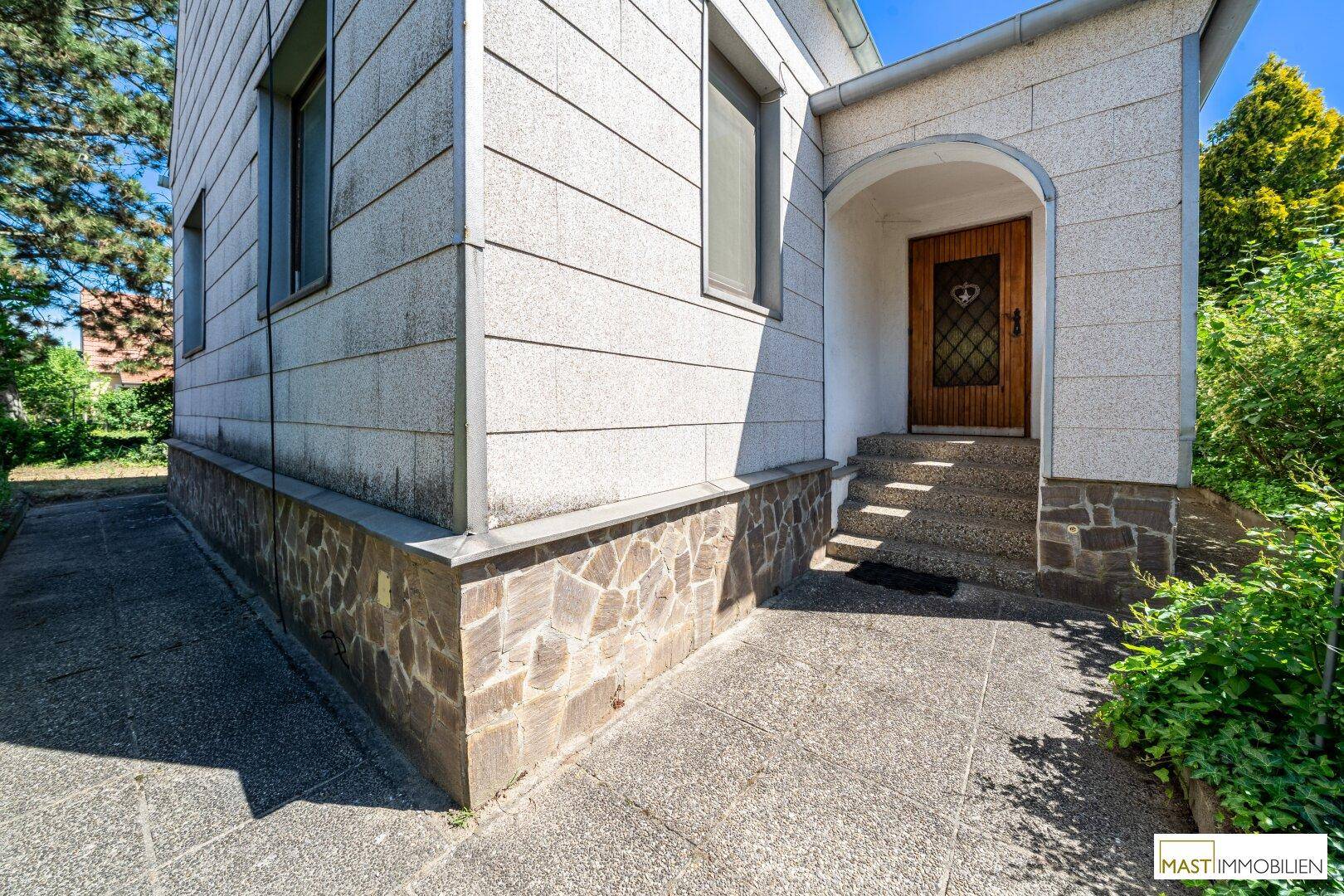 Eingangsbereich des Hauses mit Steinfassade und Treppe zur Haustür.