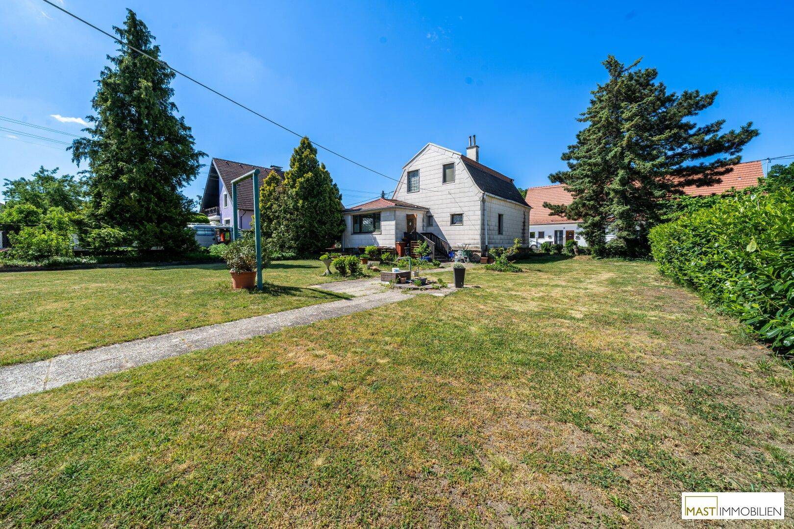 Weitläufiger Garten mit Rasenfläche und dem Haus in der Ferne unter blauem Himmel.