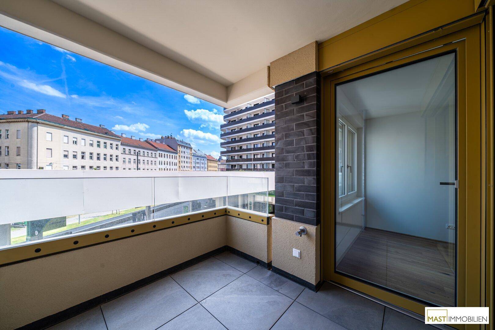 Überdachter Balkon mit Fliesenboden und Blick auf die Stadt und umliegende Gebäude.