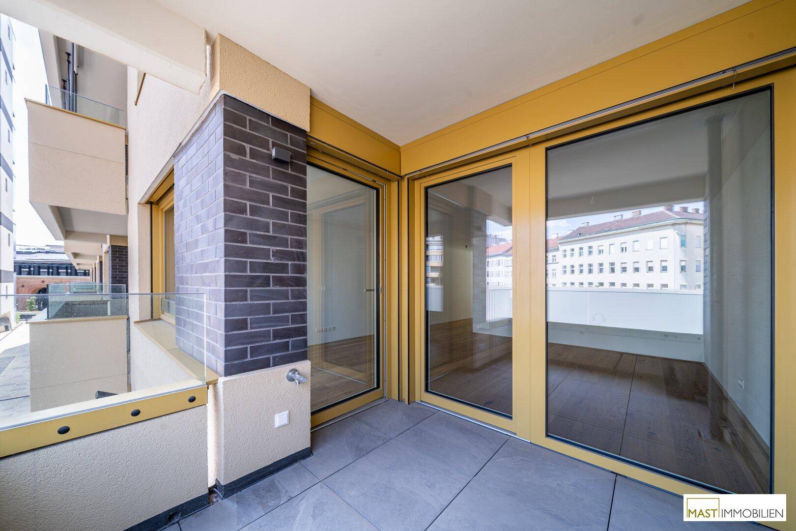 Geräumiger Balkon mit Fliesenboden und großen Fenstern, die viel Licht in die Innenräume lassen.