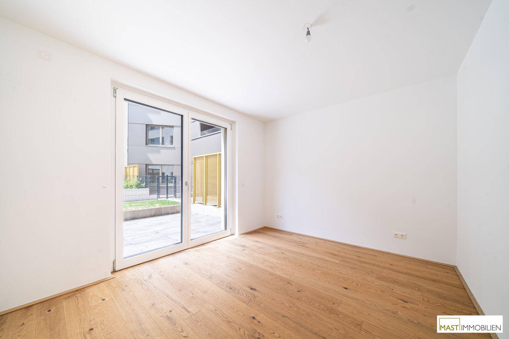 Helles Zimmer mit Parkettboden und Zugang zu einem kleinen Außenbereich oder Garten.