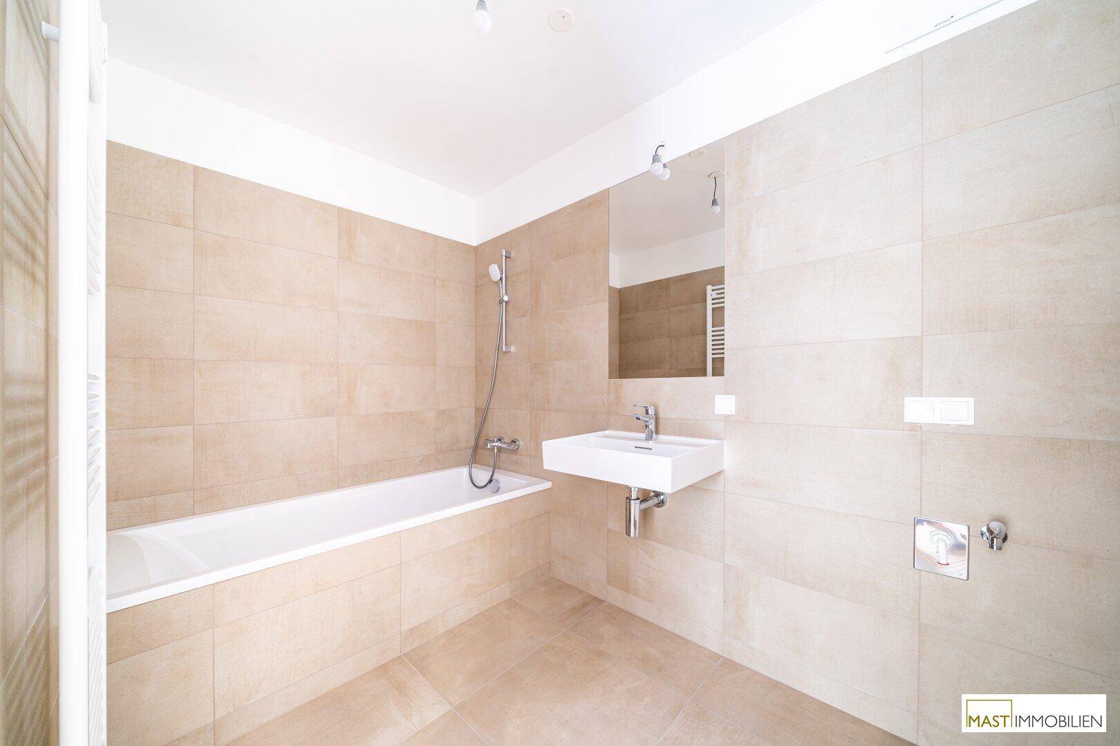 Modernes Badezimmer mit beigefarbenen Fliesen, Badewanne und wandmontiertem Waschbecken.