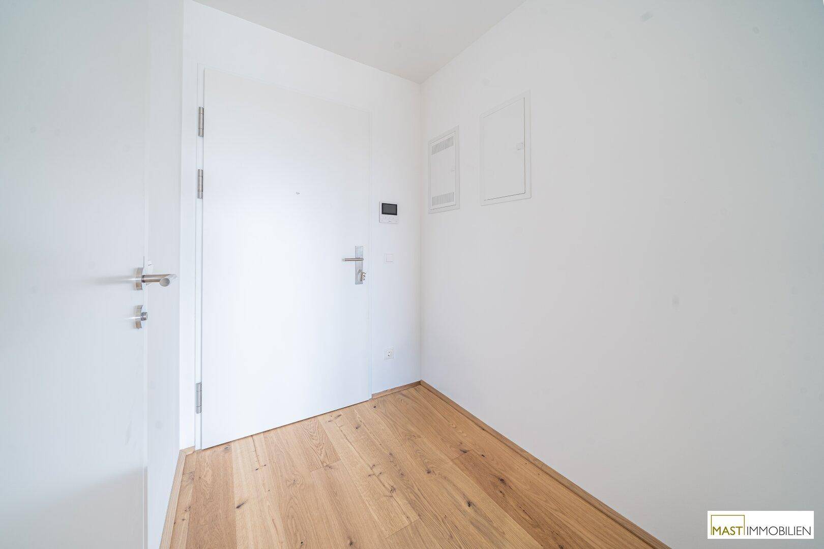 Heller Eingangsbereich mit Holzboden und weißer Tür, bietet einen freundlichen Empfang.
