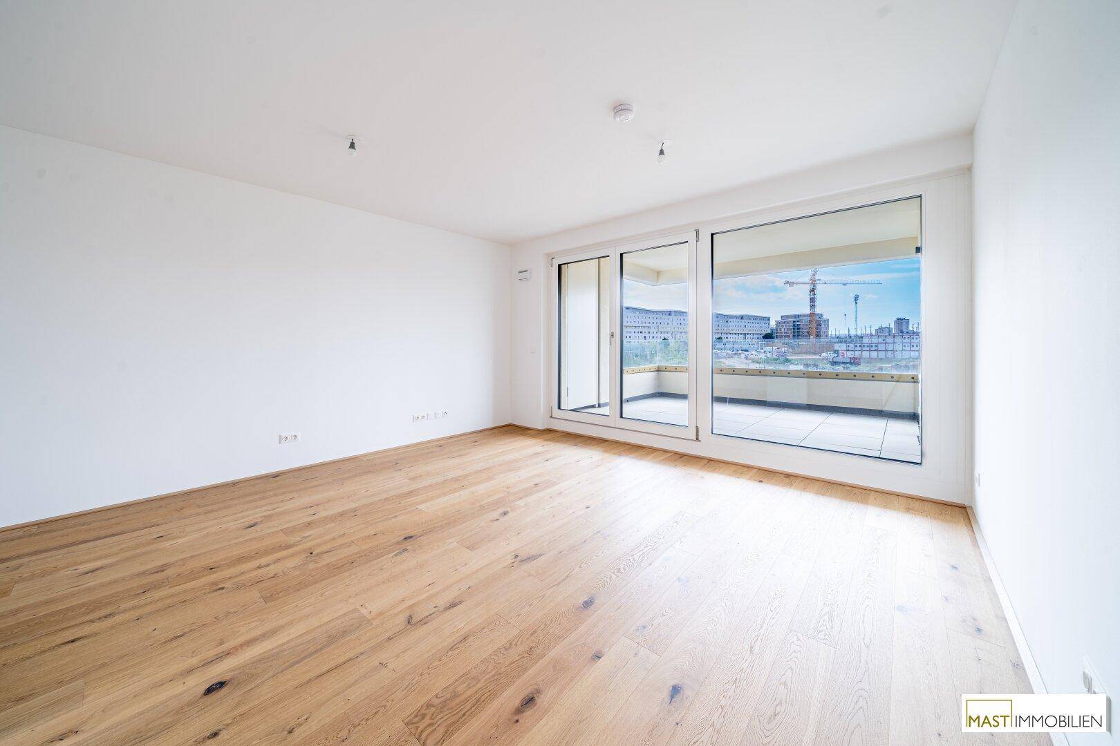 Lichtdurchfluteter Wohnraum mit Holzboden und Zugang zu einem Balkon, bietet einen Blick auf die Stadt.