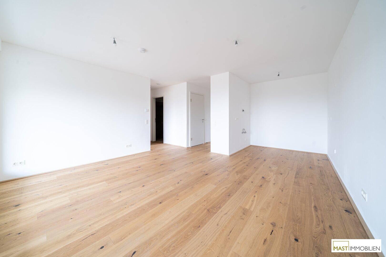 Heller, leerer Raum mit weißen Wänden und neuem Holzplankenboden, bereit zur individuellen Gestaltung.