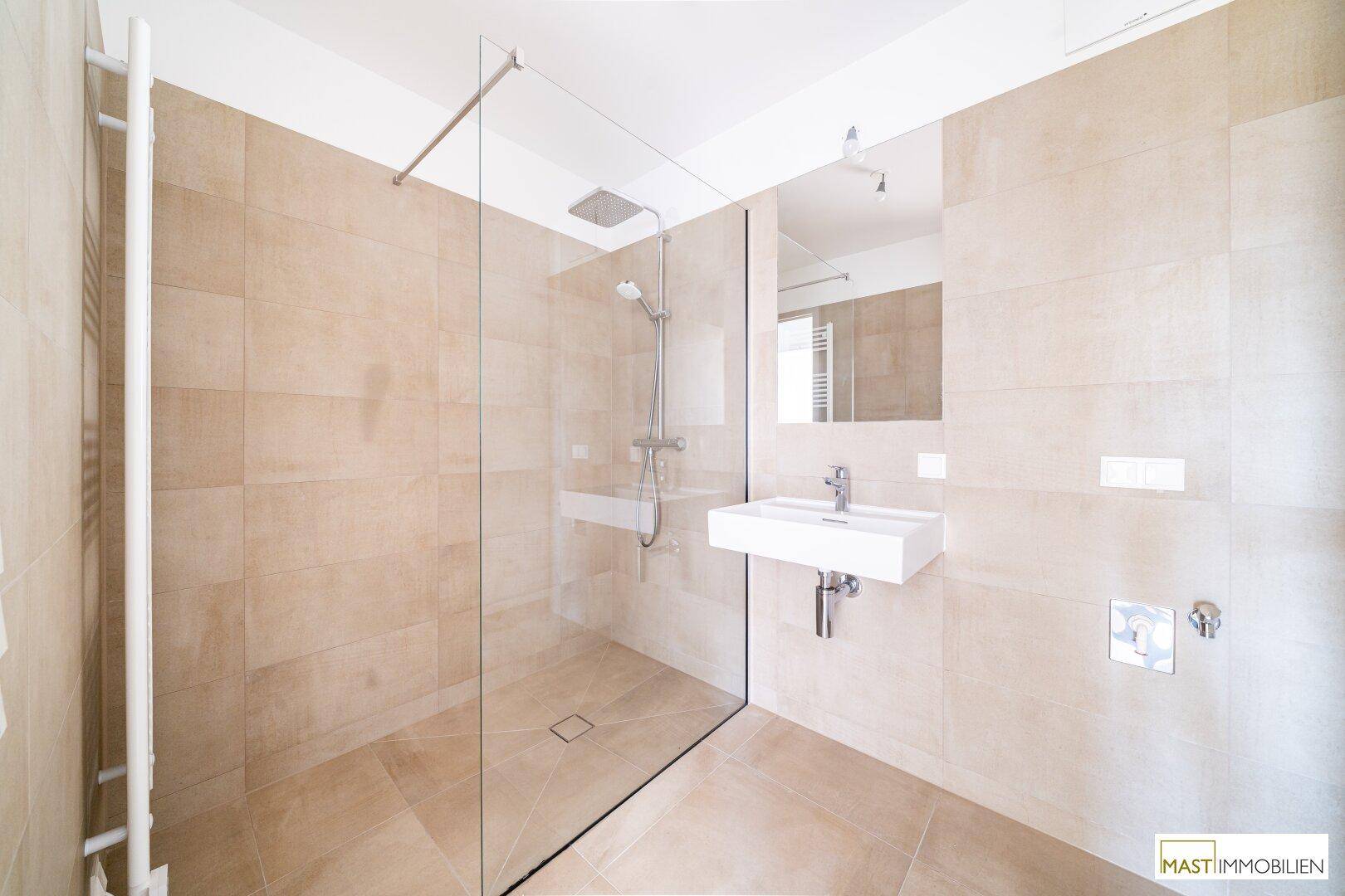 Geräumiges Badezimmer mit ebenerdiger Dusche, modernem Waschbecken und beheiztem Handtuchhalter.