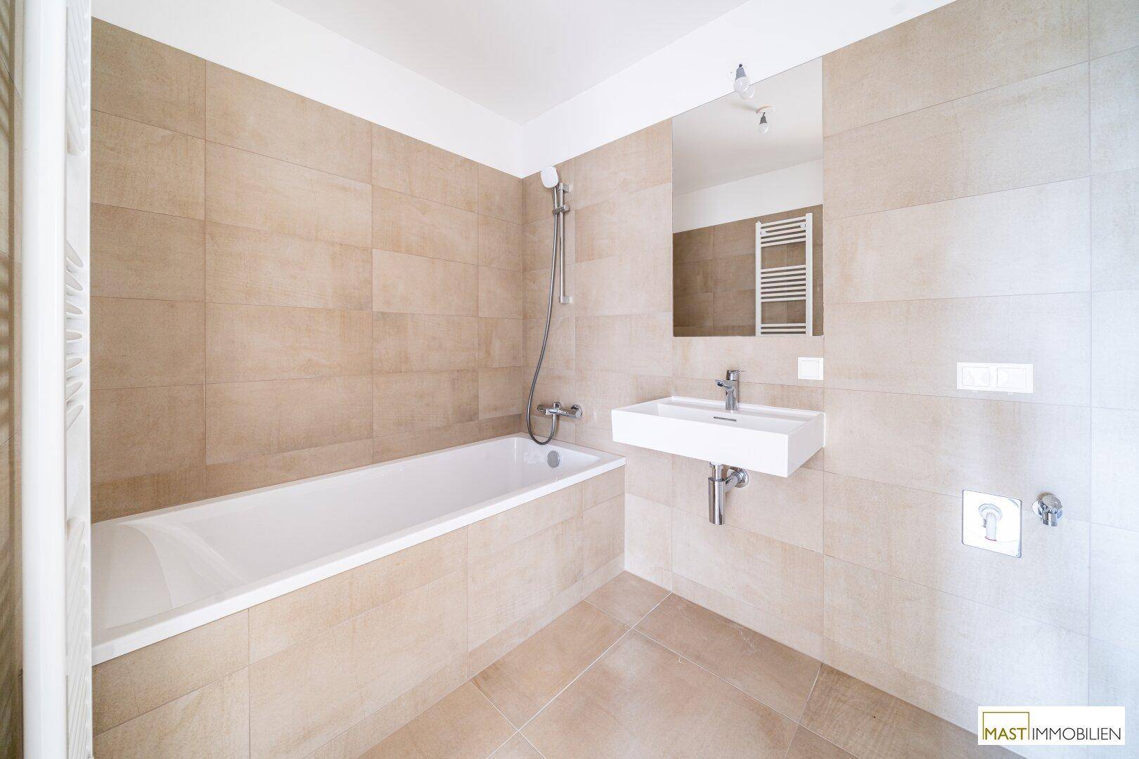 Modernes Badezimmer mit Badewanne, Waschbecken und beheiztem Handtuchhalter, in beigen Fliesen gehalten.