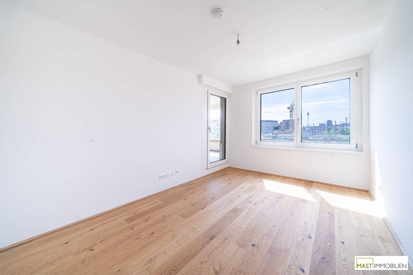 Heller Raum mit großen Fenstern und Holzboden, bietet viel Tageslicht und einen Ausblick.