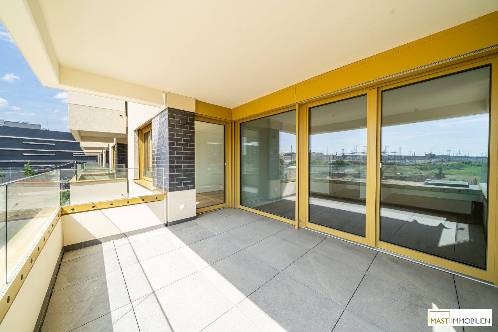 Heller Balkon mit großen Glasfronten und Fliesenboden, bietet viel Sonnenlicht und einen weiten Blick.