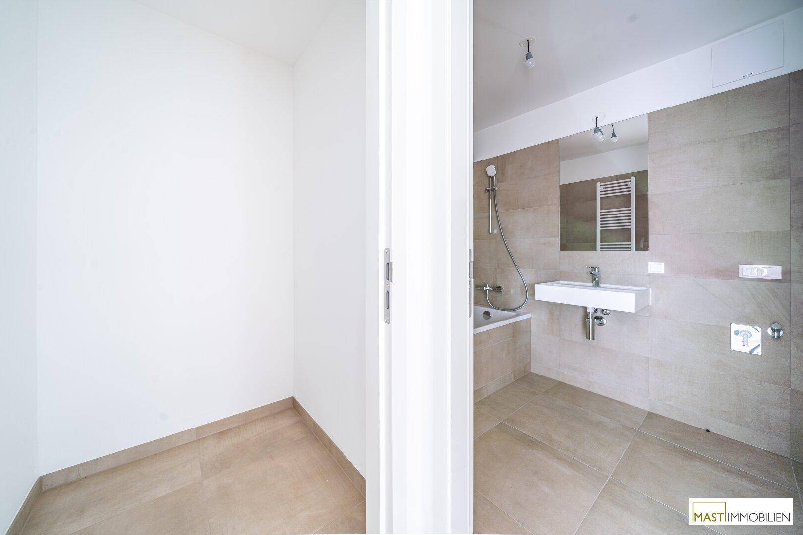 Modernes Badezimmer mit beigefarbenen Fliesen, Badewanne mit Duschfunktion und einem Waschbecken.