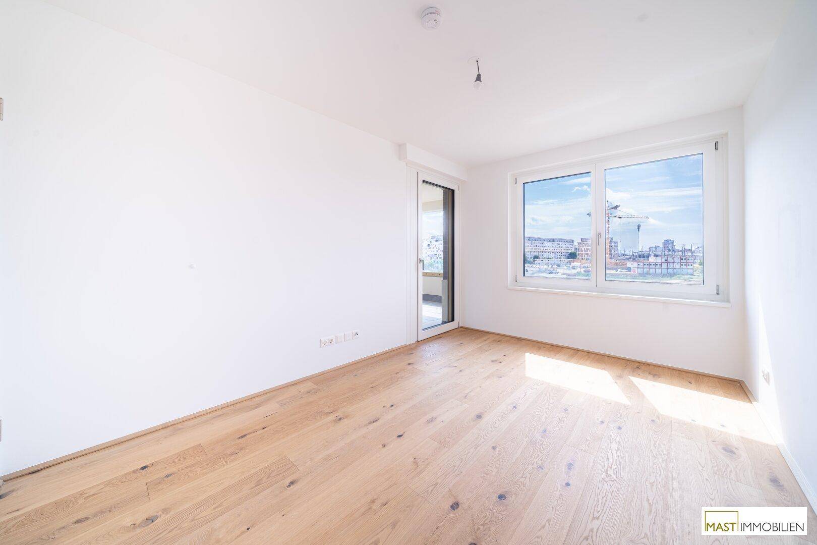 Helles Schlafzimmer mit Parkettboden und Fenster, das Zugang zu einem Balkon mit Stadtblick bietet.
