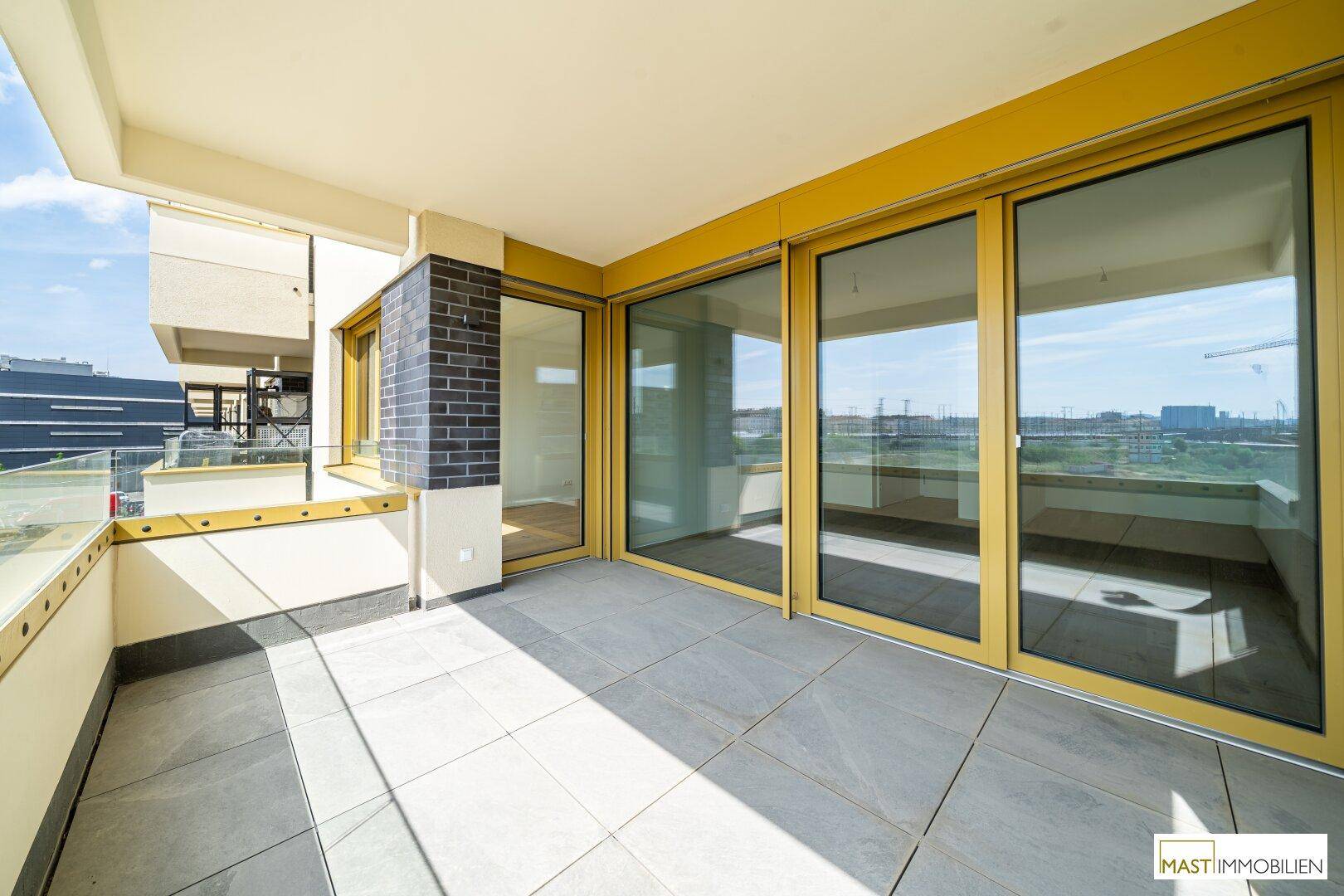 Großer Balkon mit Fliesenboden und breiten Glasfronten, bietet einen weiten Blick auf die Umgebung.