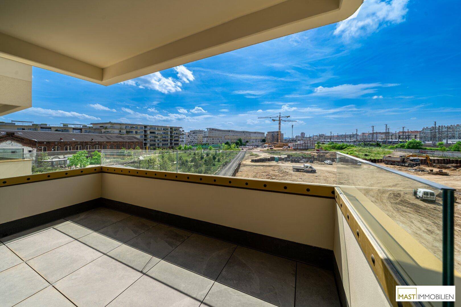Sonniger Balkon mit Fliesenboden und Glasgeländer, ideal für Entspannung mit Blick auf die Stadt.