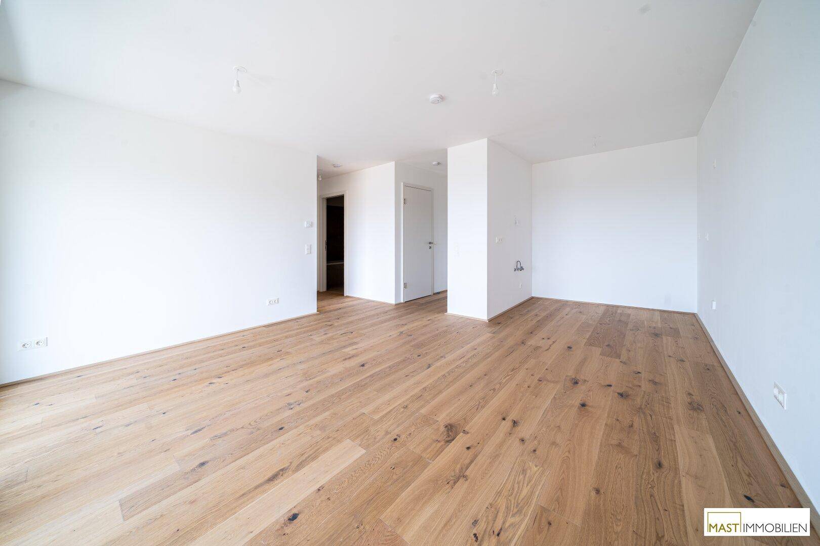 Großes, leeres Zimmer mit Holzboden und weißen Wänden, bereit für individuelle Gestaltung und Einrichtung.