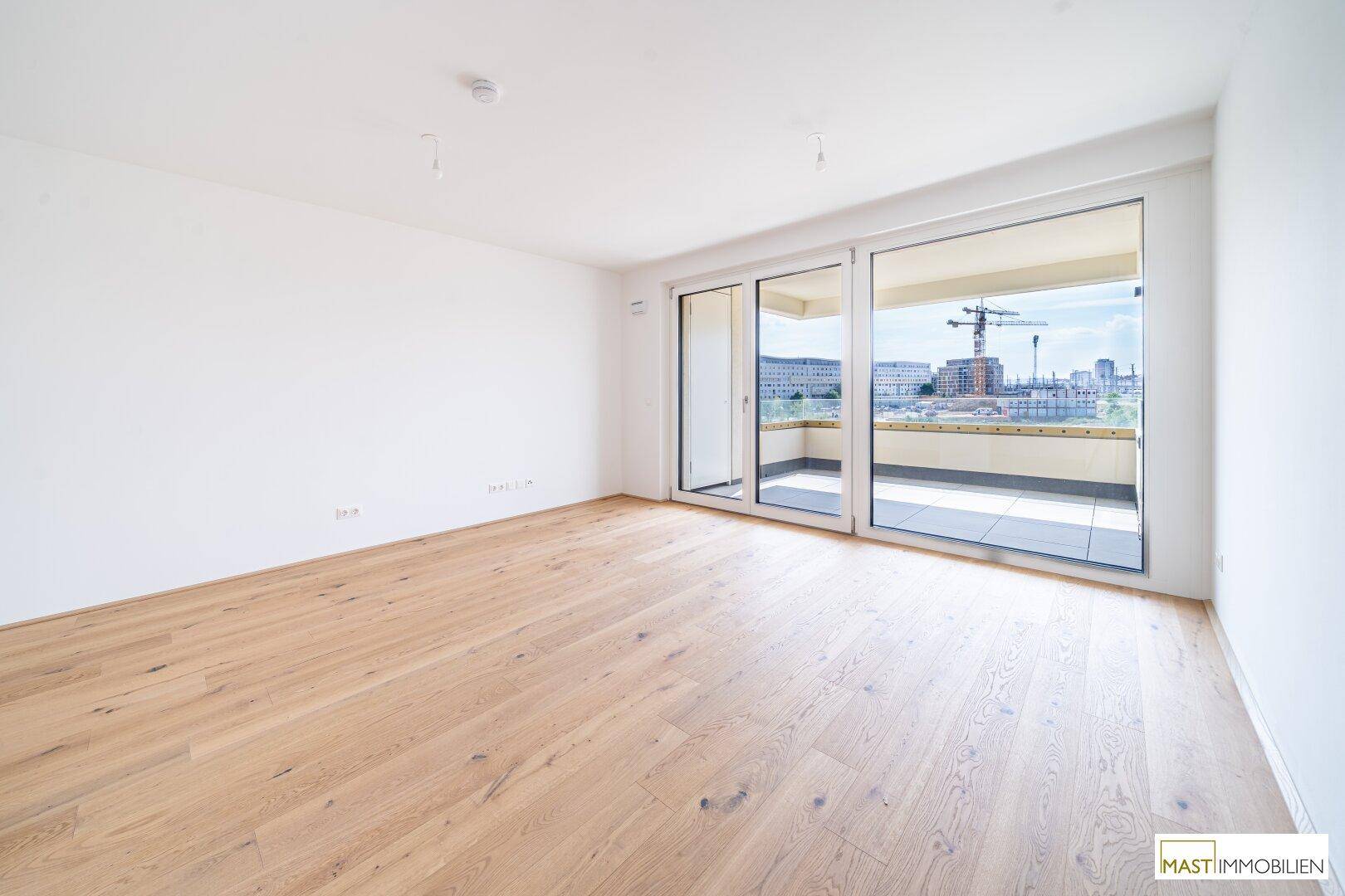 Geräumiges, helles Zimmer mit Holzboden und Zugang zu einem Balkon, ideal für offenes Wohnen.