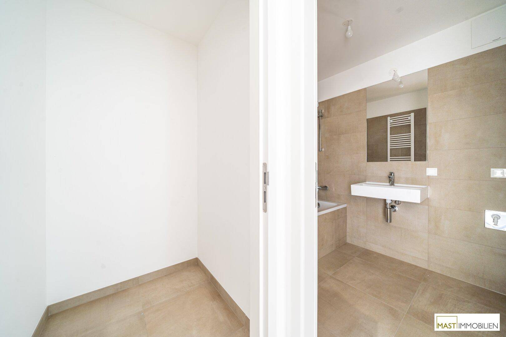 Modernes Badezimmer mit beigefarbenen Fliesen, Waschbecken und Spiegel, teilweise sichtbar.