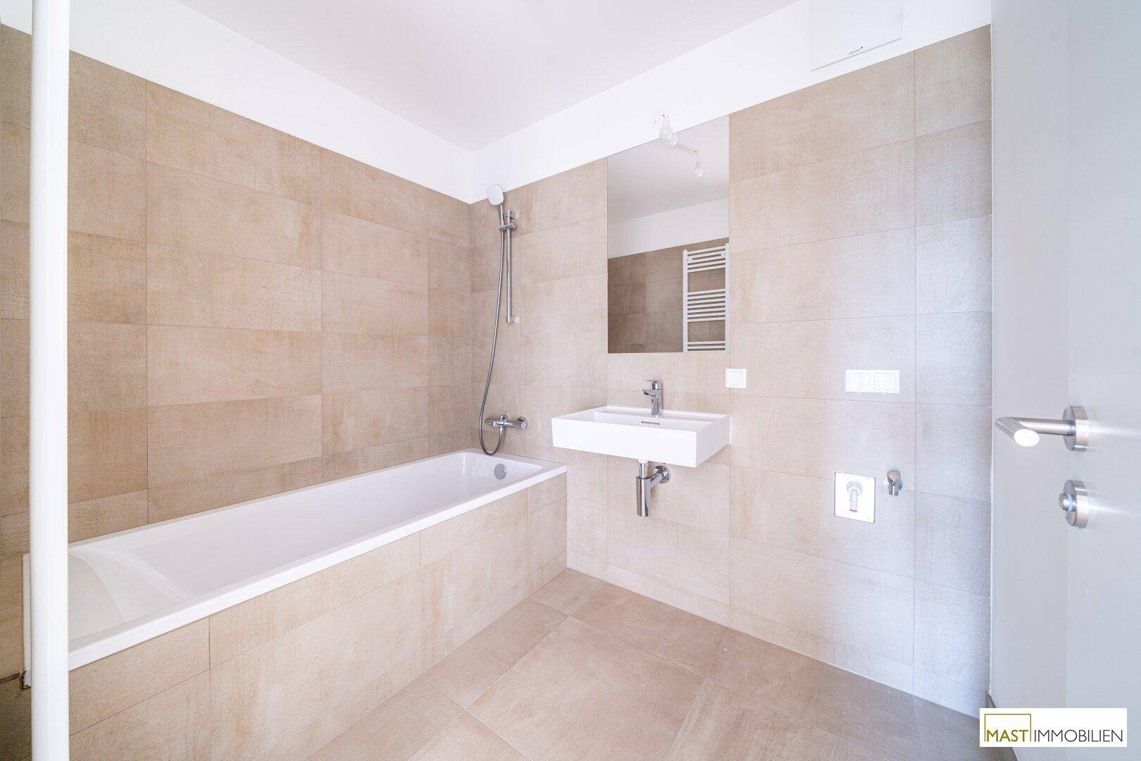 Helles Badezimmer mit Badewanne, Waschbecken, Spiegel und beheiztem Handtuchhalter, in neutralen Farbtönen gehalten.