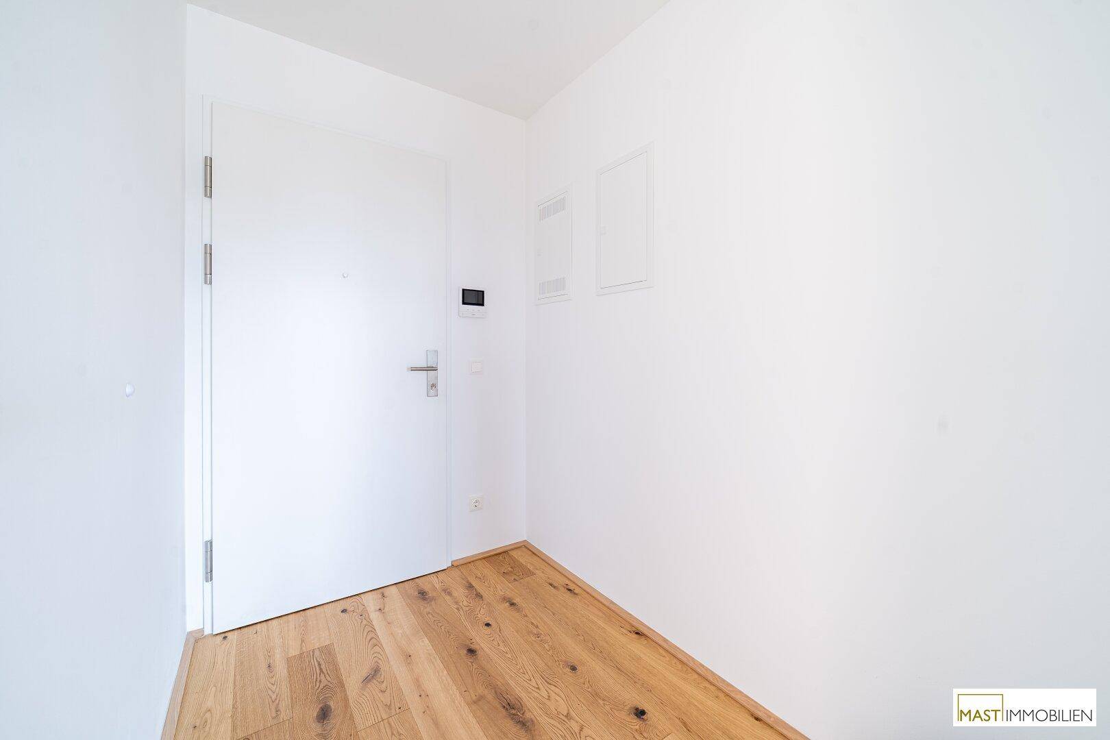 Heller Eingangsbereich mit Holzboden und weißer Tür, wirkt modern und einladend.