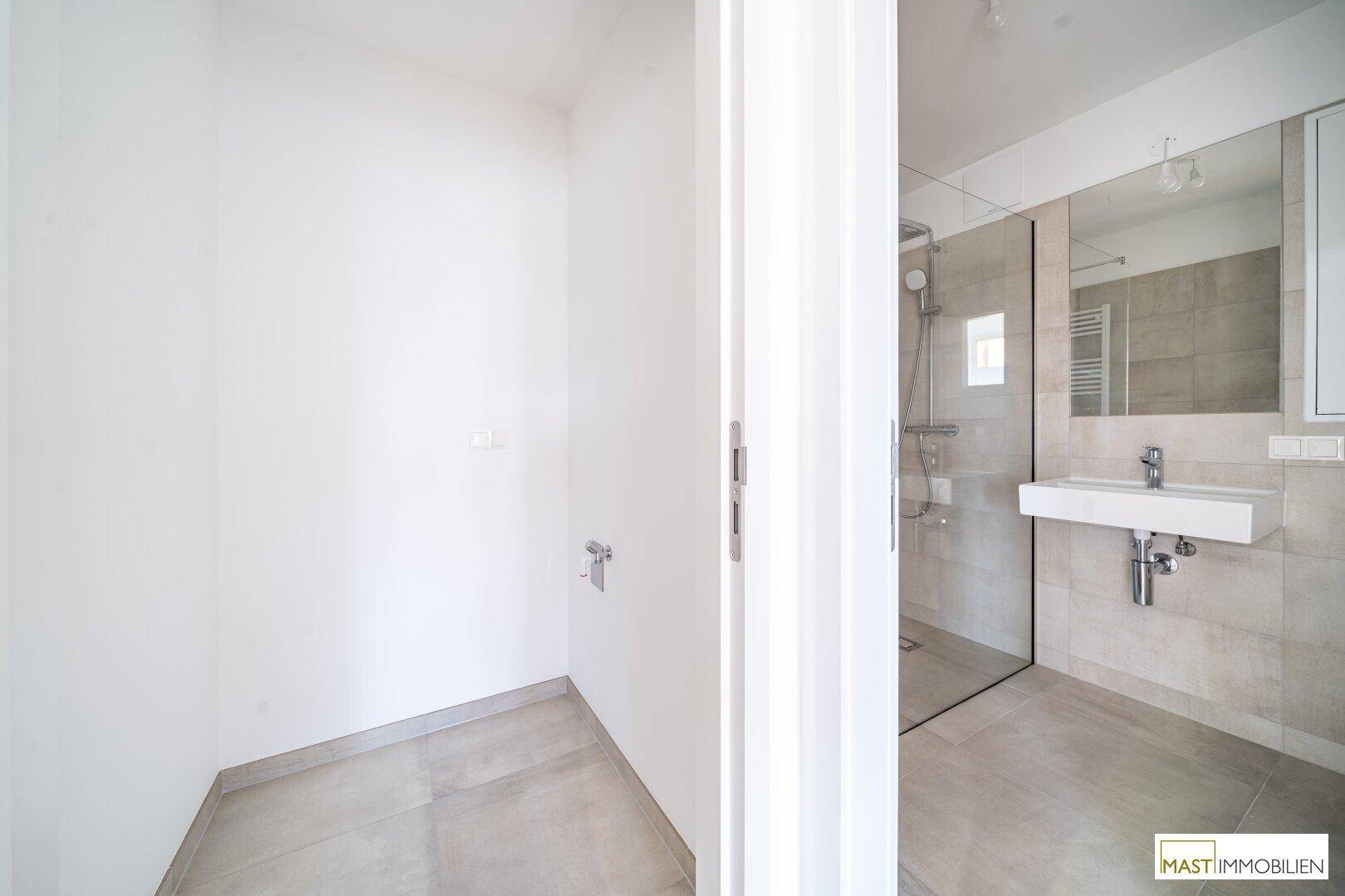 Modernes Badezimmer mit Duschbereich und Waschbecken, durch eine Tür getrennt.