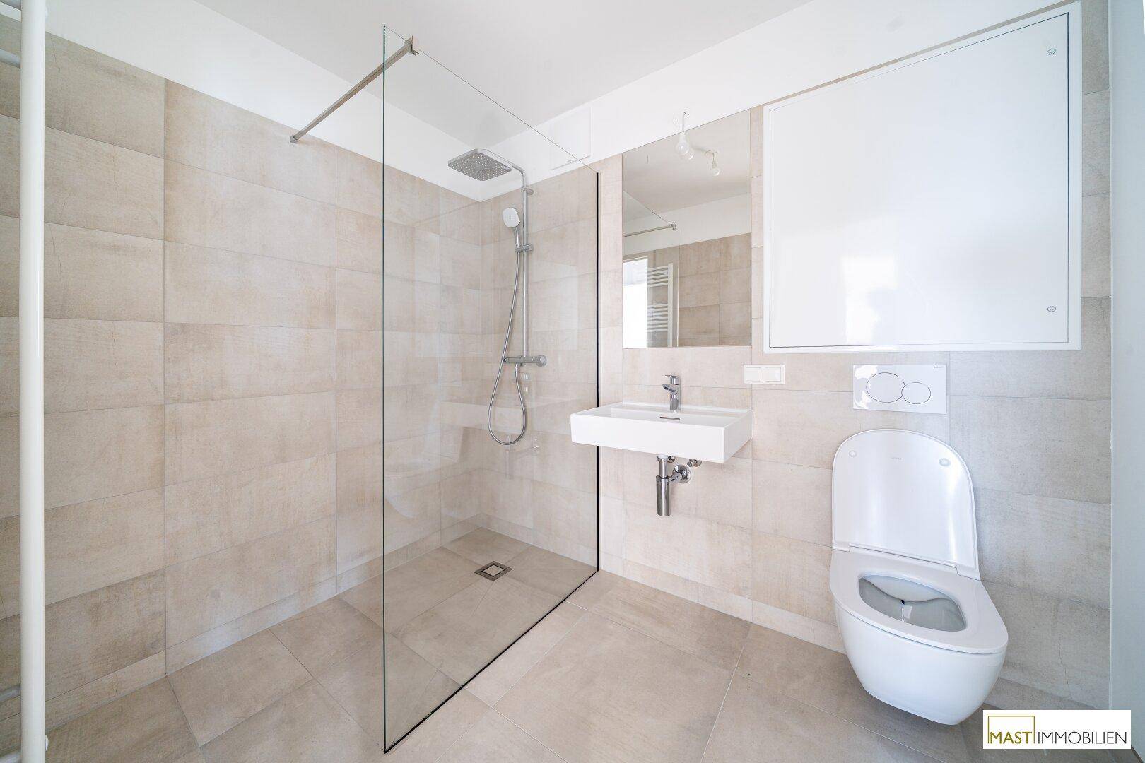 Modernes Badezimmer mit ebenerdiger Dusche, WC und Waschbecken, hell gefliest.