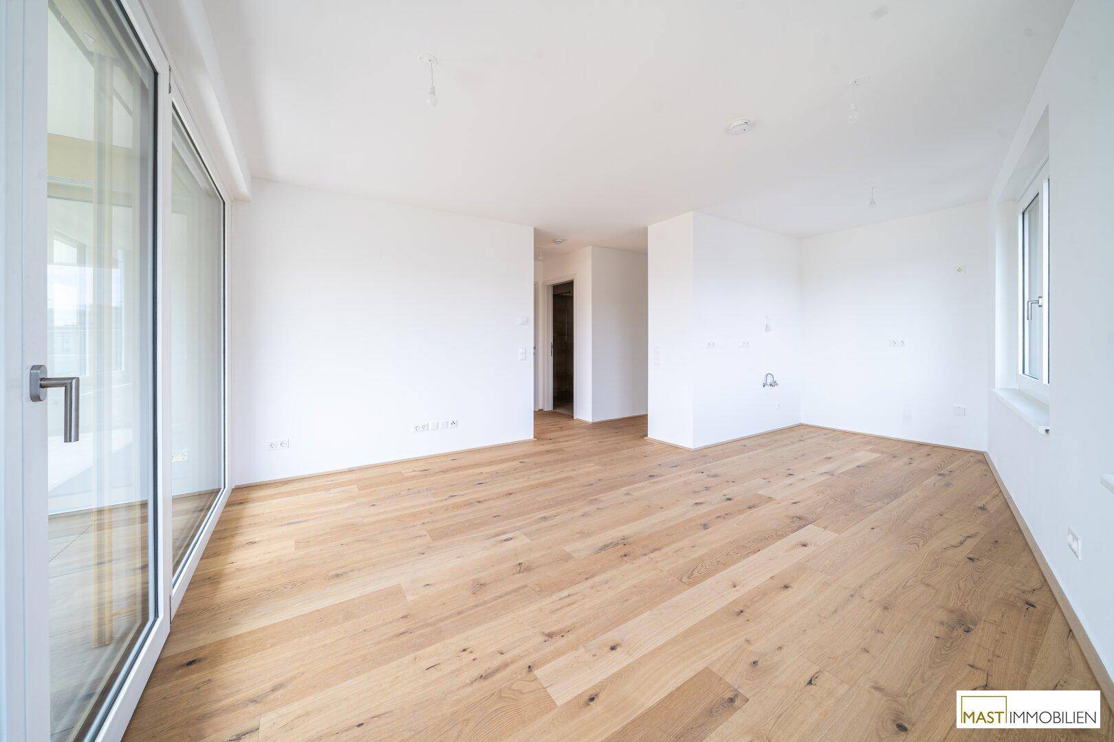 Großzügiger, heller Raum mit Holzboden und Zugang zu einem Balkon, ideal für offenes Wohnen.
