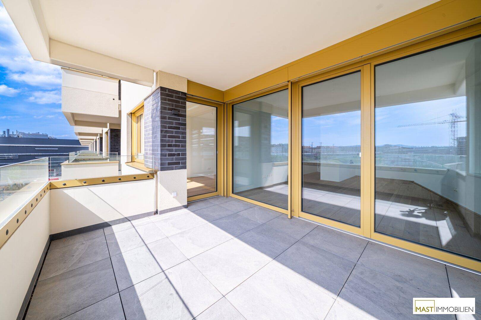 Langer Balkon mit Fliesenboden und Glasgeländer, bietet viel Sonnenlicht und Weitblick.