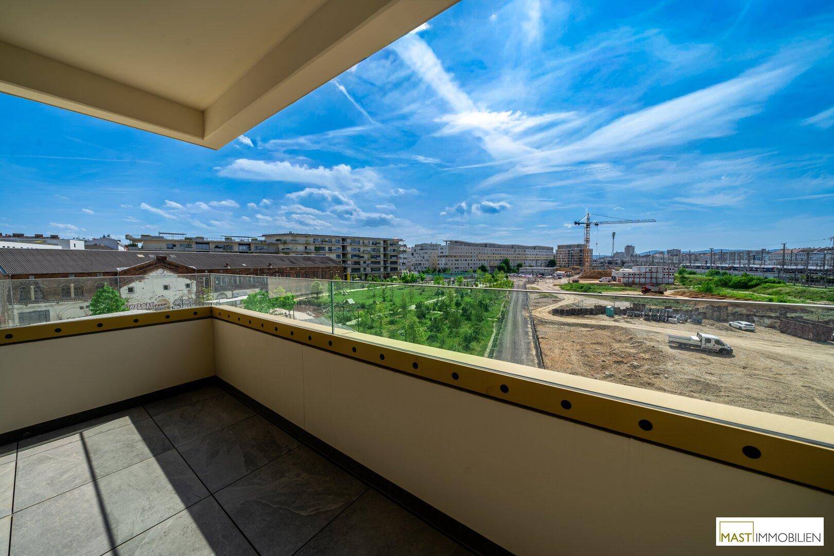 Sonniger Balkon mit Fliesenboden und Glasgeländer, bietet einen weiten Blick über die Umgebung.