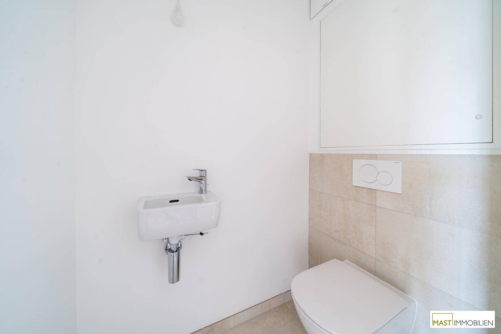 Separates Gäste-WC mit wandhängender Toilette und kleinem Waschbecken, in schlichtem Design.
