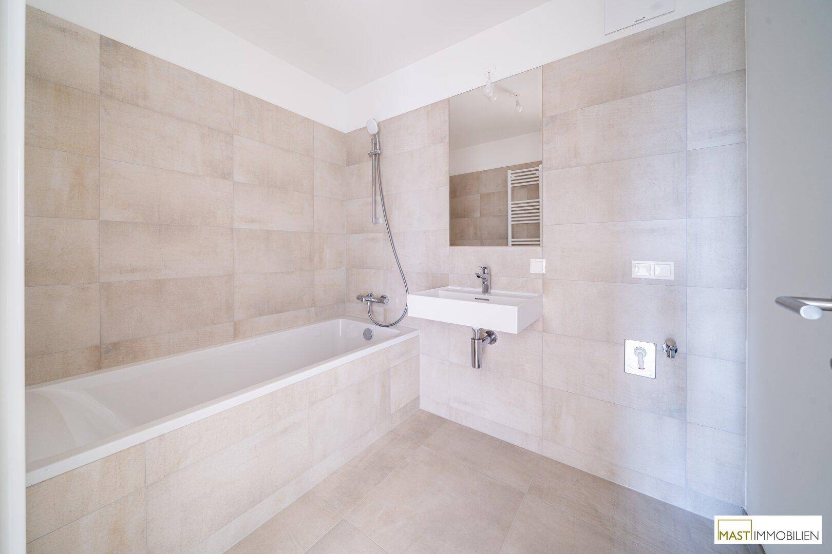 Helles Badezimmer mit Badewanne, modernem Waschbecken und großem Spiegel, in neuwertigem Zustand.