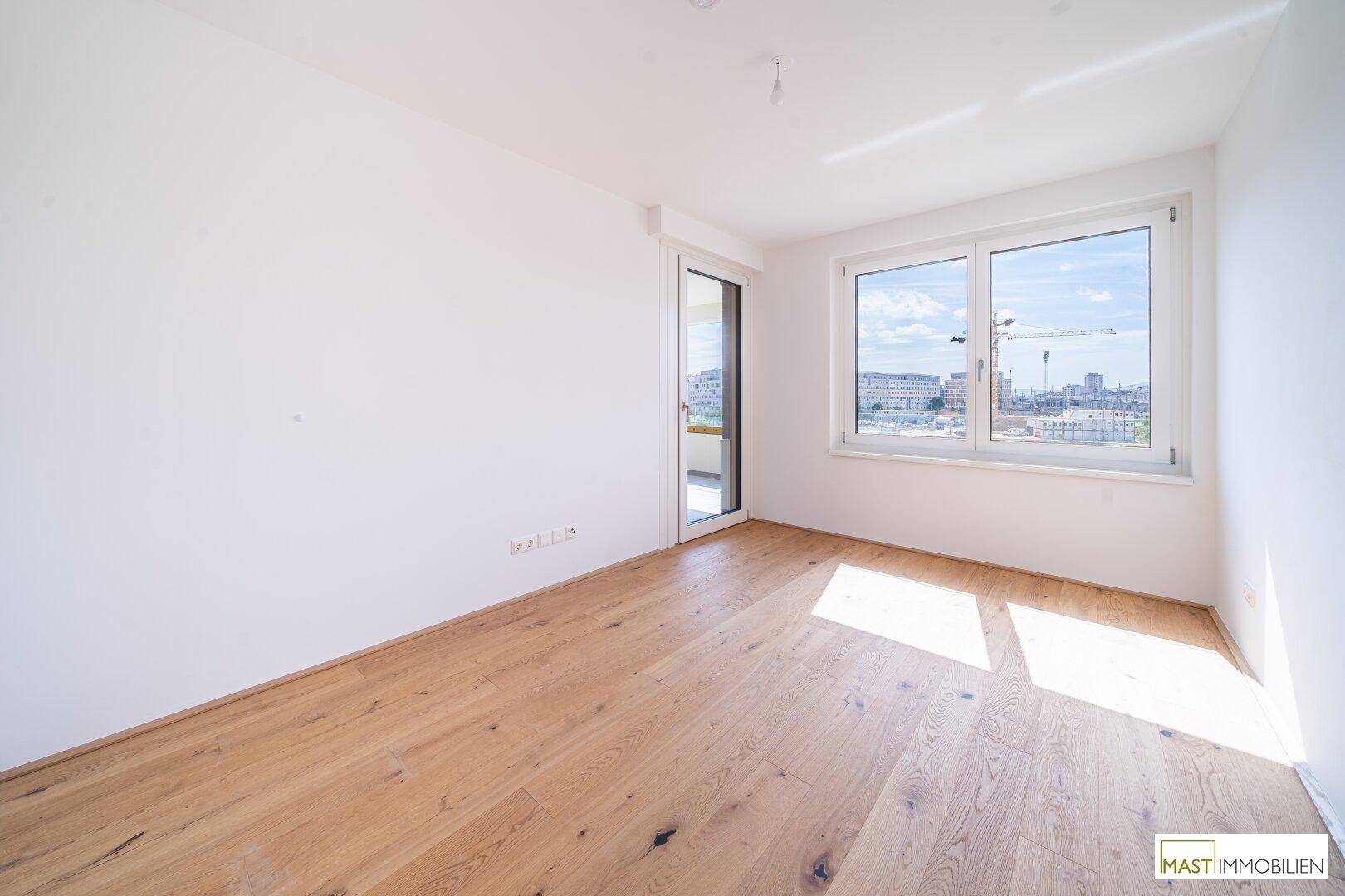 Lichtdurchflutetes Zimmer mit Parkettboden und großen Fenstern, bietet einen weiten Blick nach draußen.