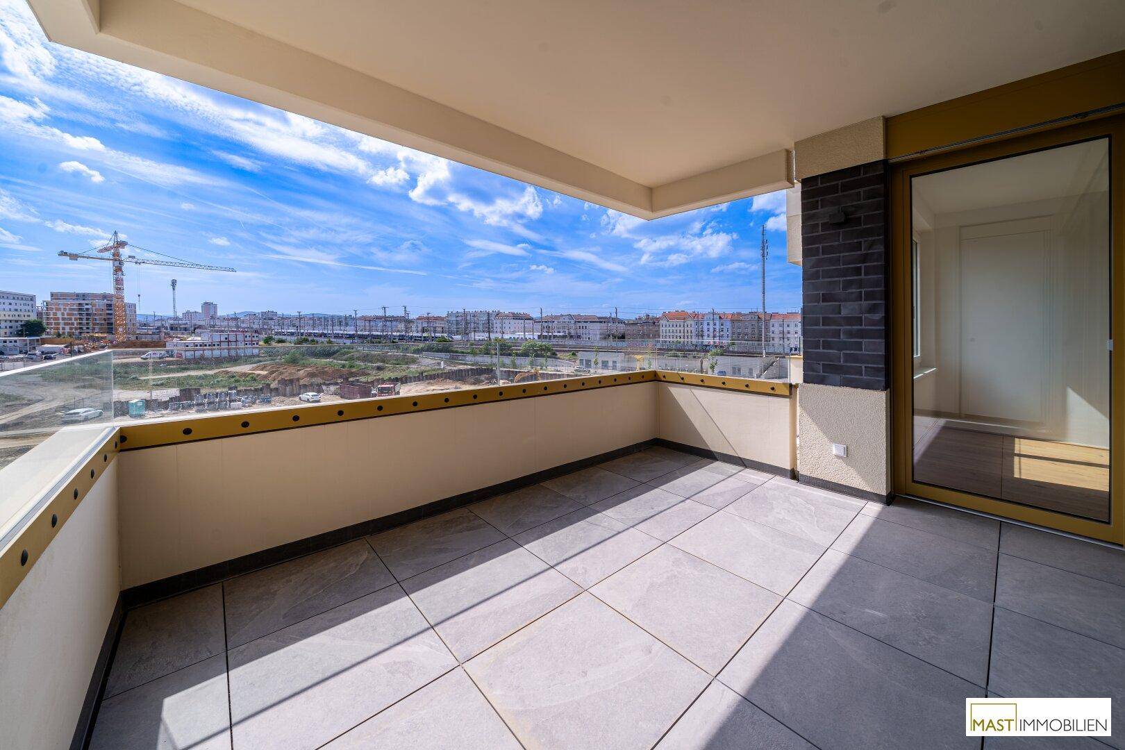 Geräumiger Balkon mit Fliesenboden und Glasgeländer, bietet einen weiten Blick über die Stadt.