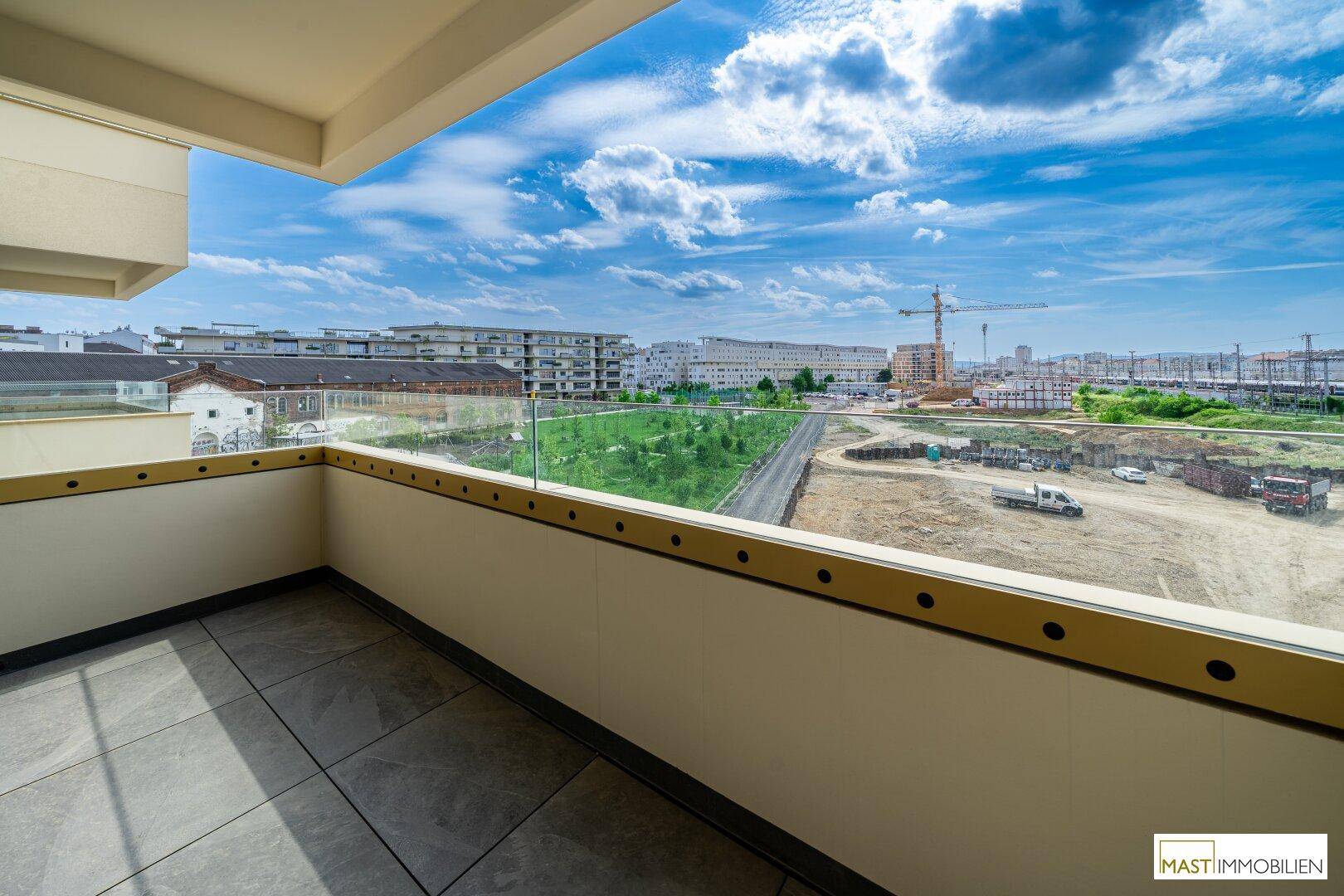 Weitläufiger Balkon mit Glasgeländer und Blick auf die umliegende Stadtlandschaft und Grünflächen.