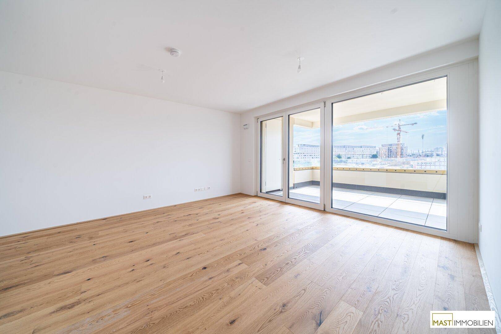 Leerer Raum mit hellem Holzboden und großen Schiebetüren, die auf einen Balkon führen.