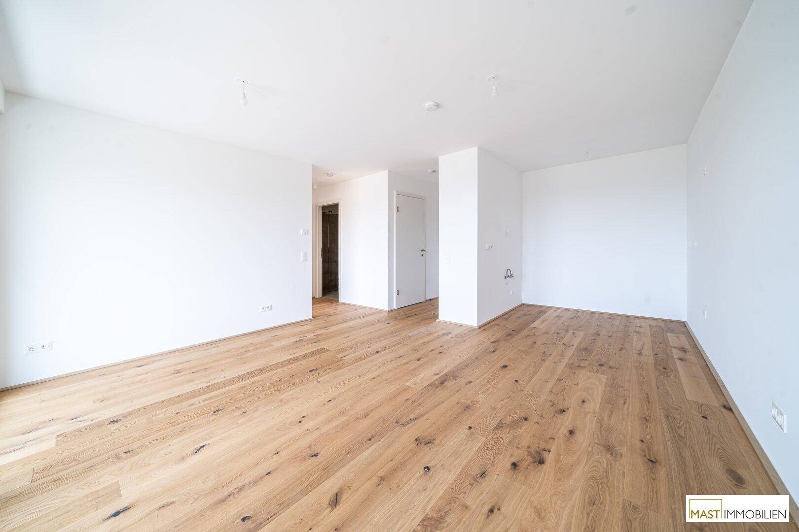 Heller, leerer Raum mit Holzboden und Zugang zu einem Flur, ideal für individuelle Gestaltung.