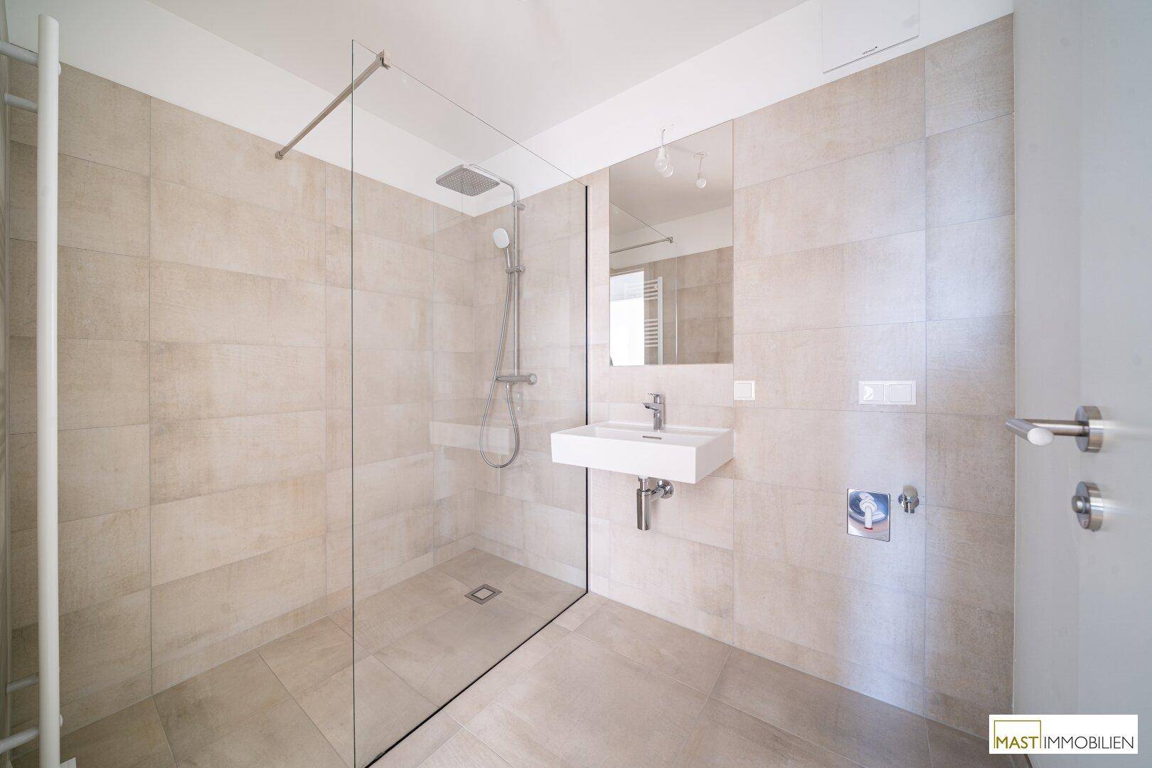 Modernes Badezimmer mit großer begehbarer Dusche, elegantem Waschbecken und hellen Wandfliesen.