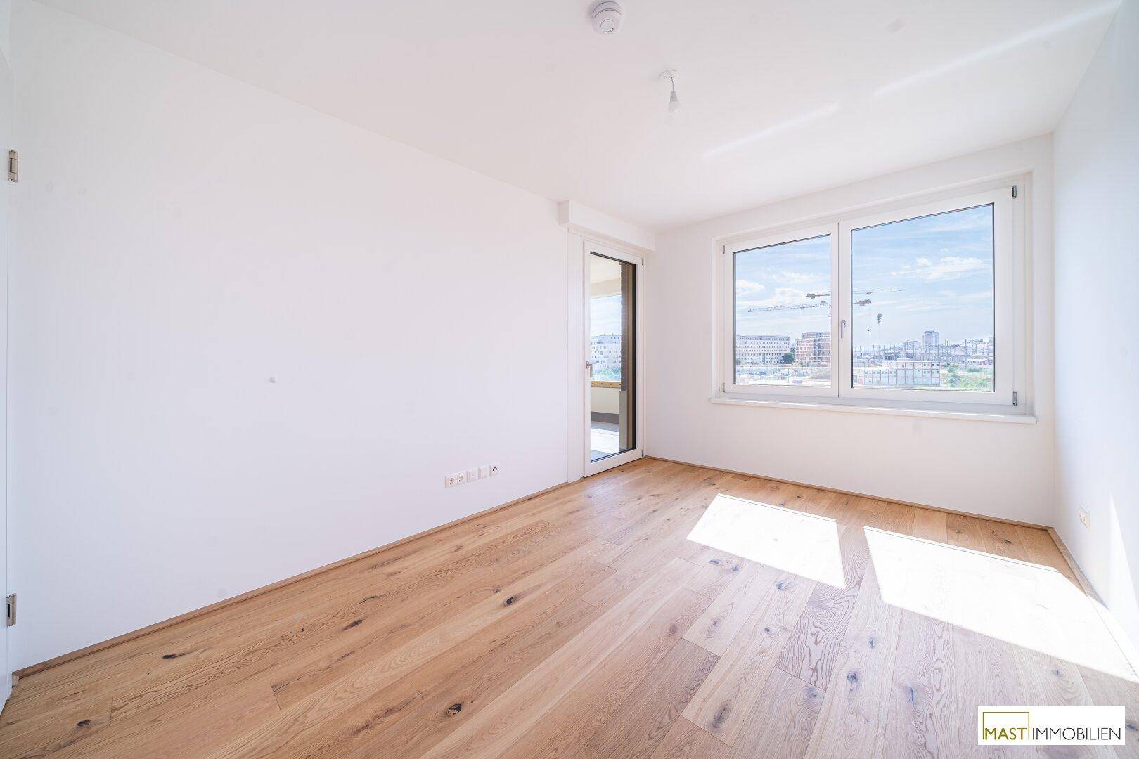 Helles Schlafzimmer mit Holzboden, großem Fenster und Zugang zu einem Außenbereich, sonnendurchflutet.