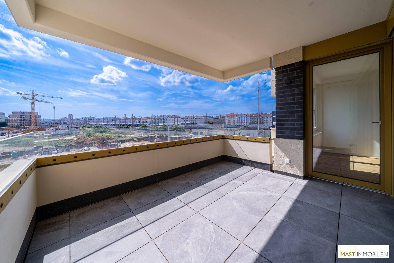 Geräumiger Balkon mit Fliesenboden und Glasgeländer, bietet einen weiten Blick auf die Stadtentwicklung.