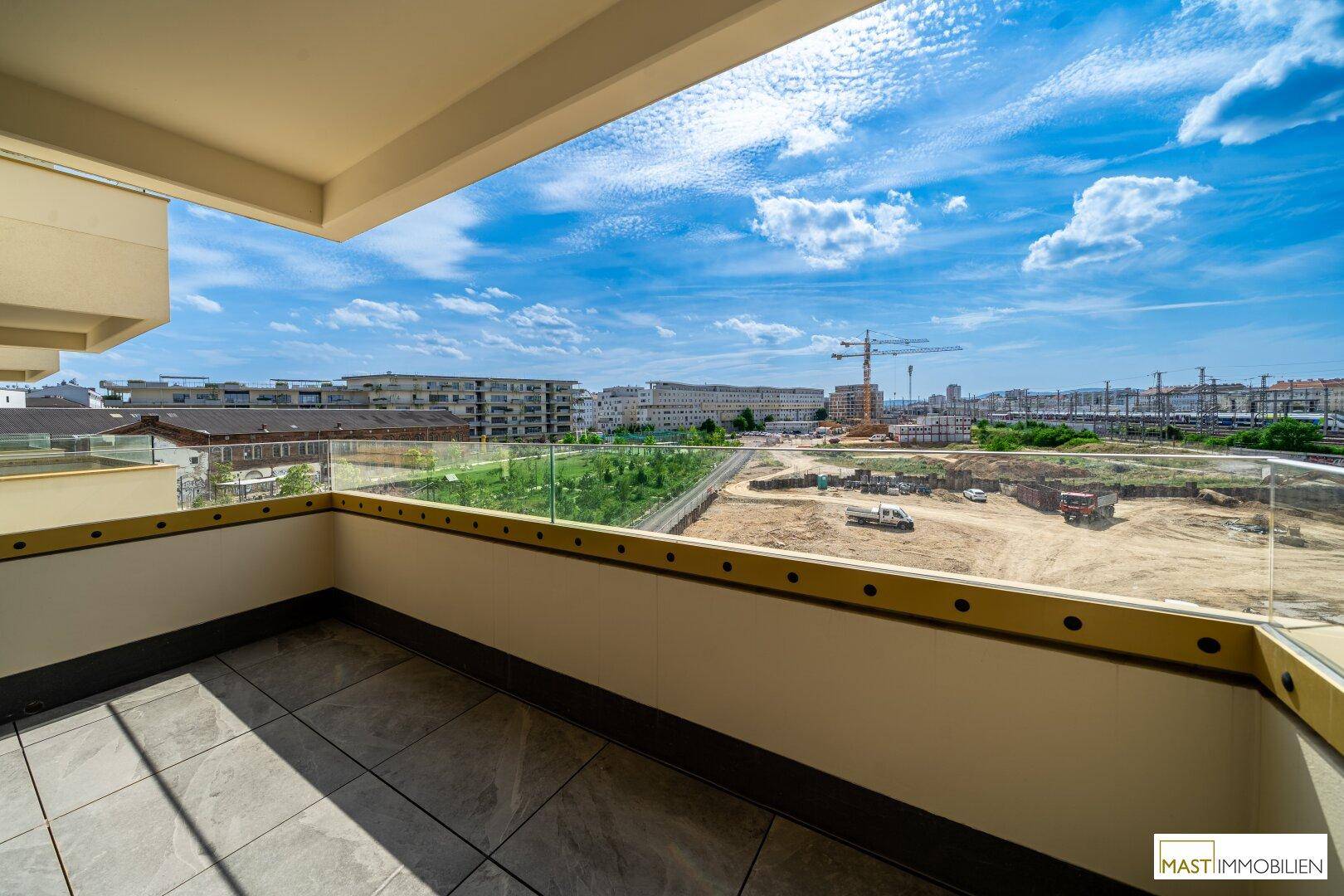 Heller Balkon mit Fliesenboden und Glasgeländer, bietet einen weiten Blick auf die städtische Umgebung.