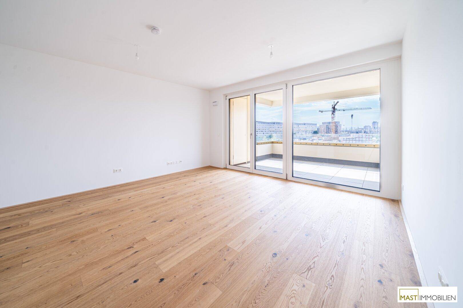 Heller, leerer Raum mit Eichenparkett und großen Schiebetüren zum Balkon, ideal für ein Wohnzimmer.