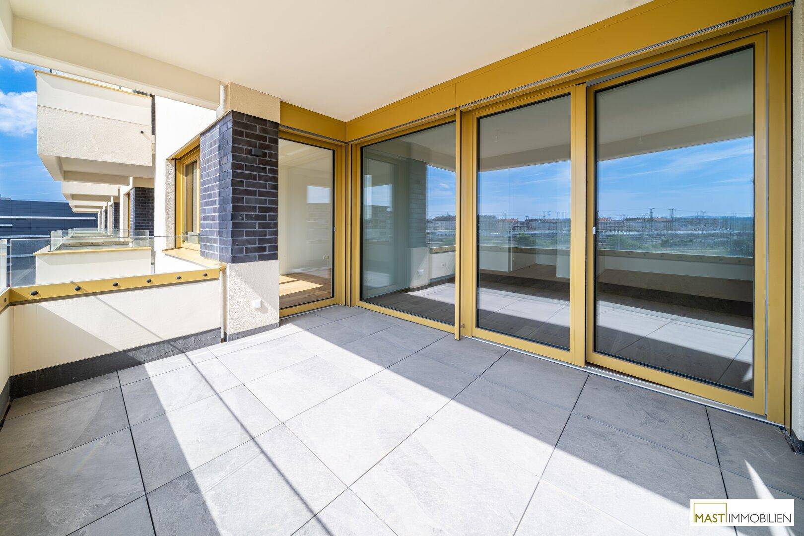 Heller Balkon mit Fliesenboden und großen Glasfronten, bietet einen weiten Blick auf die Stadt.