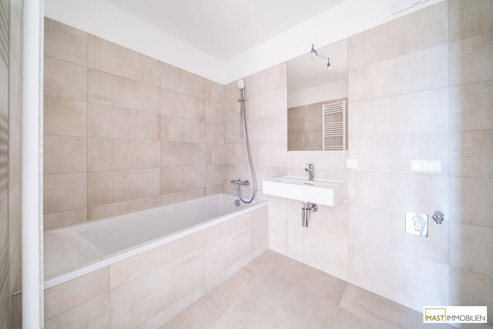 Helles Badezimmer mit Badewanne, modernem Waschbecken und großem Spiegel, komplett gefliest.