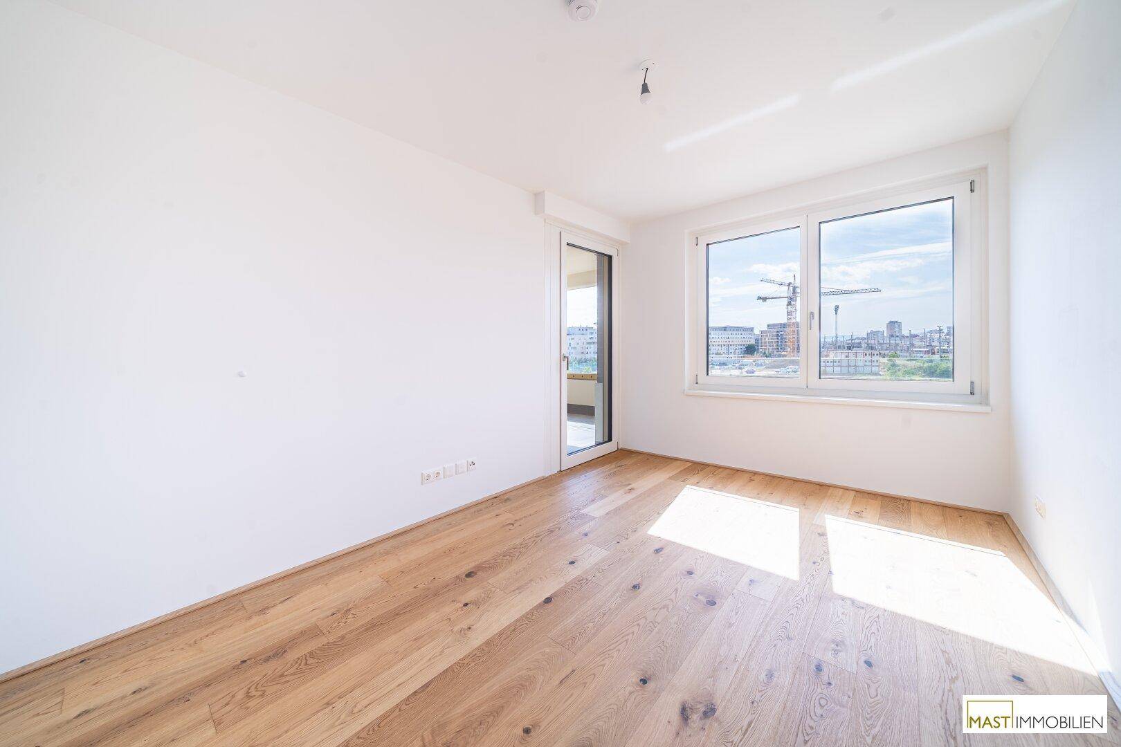 Lichtdurchfluteter Raum mit hellem Parkettboden und Fenster, bietet Zugang zu einem Außenbereich.