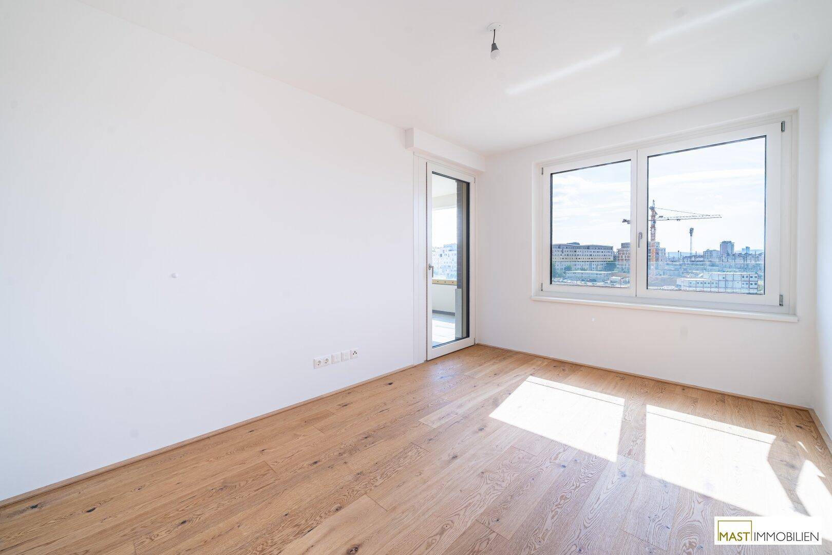 Lichtdurchflutetes Zimmer mit Holzboden und großem Fenster mit Blick auf die Stadt.