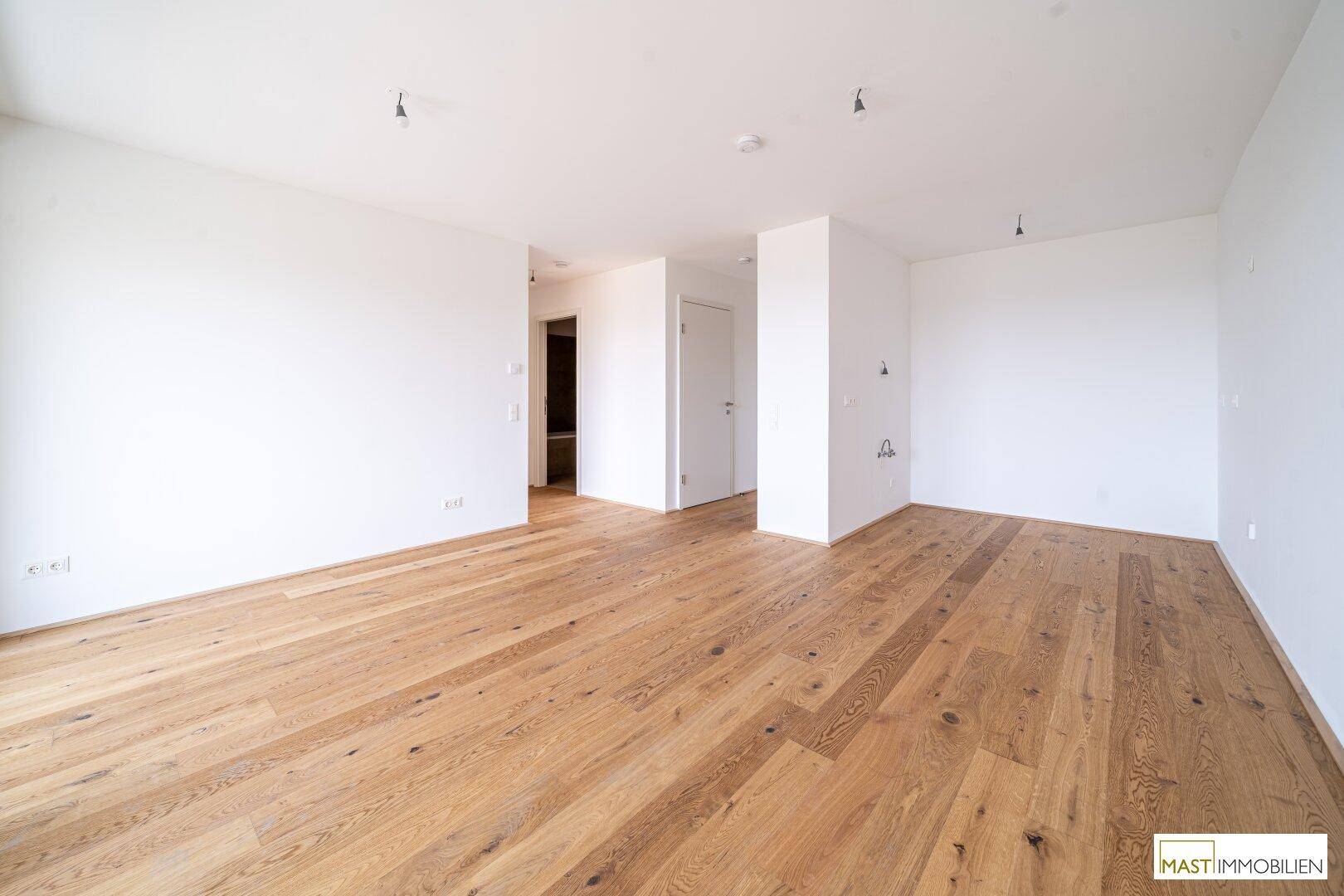 Geräumiges, helles Zimmer mit Parkettboden und weiß gestrichenen Wänden, Blick in den Flur.