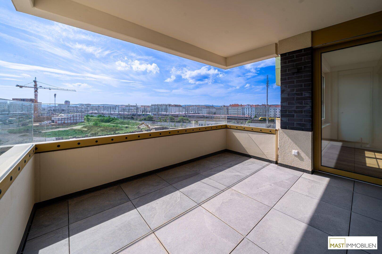 Geräumiger Balkon mit Fliesenboden und Glasgeländer, bietet einen weiten Stadtblick.