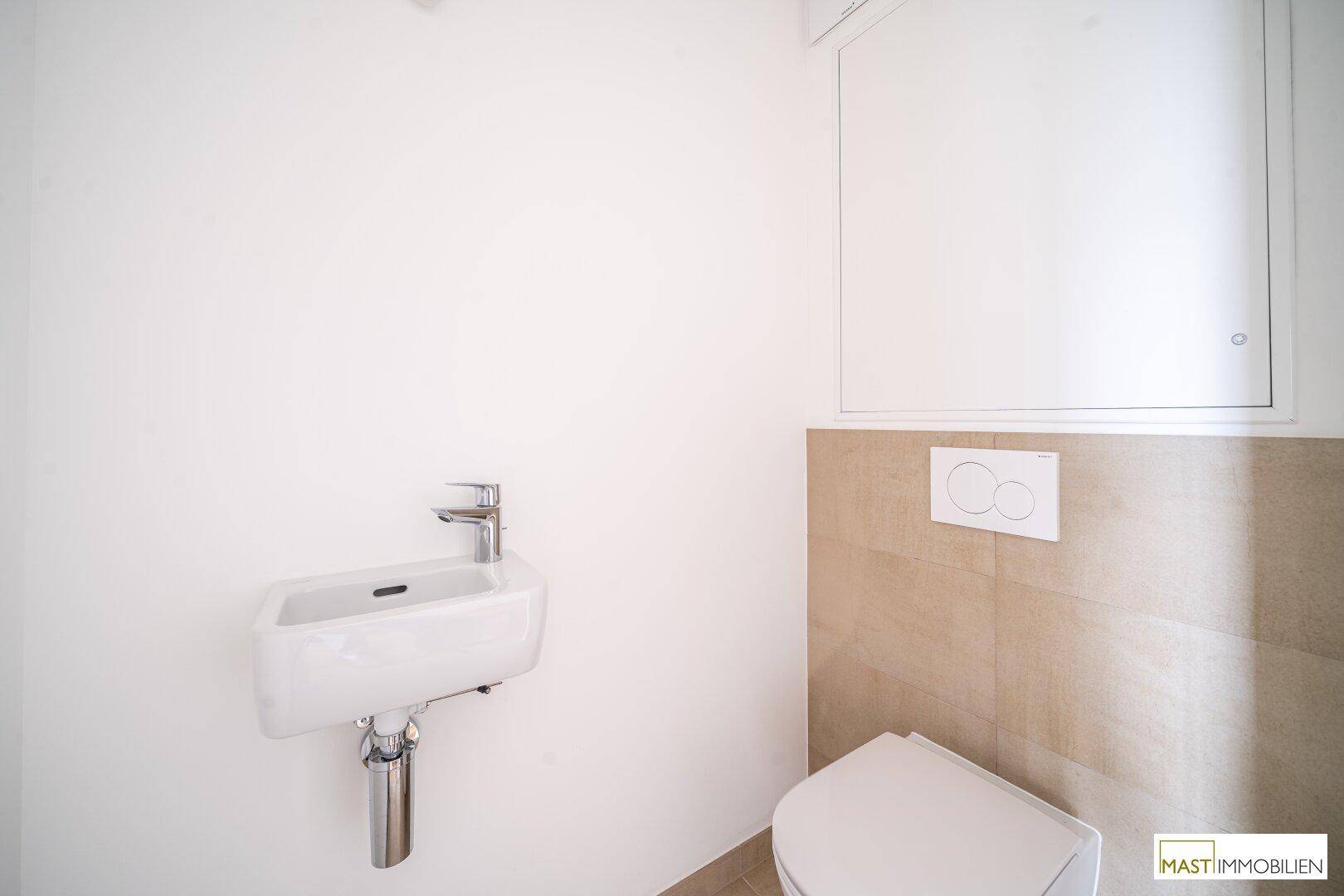 Separates WC mit wandhängender Toilette und kleinem Handwaschbecken, in modernem Design.