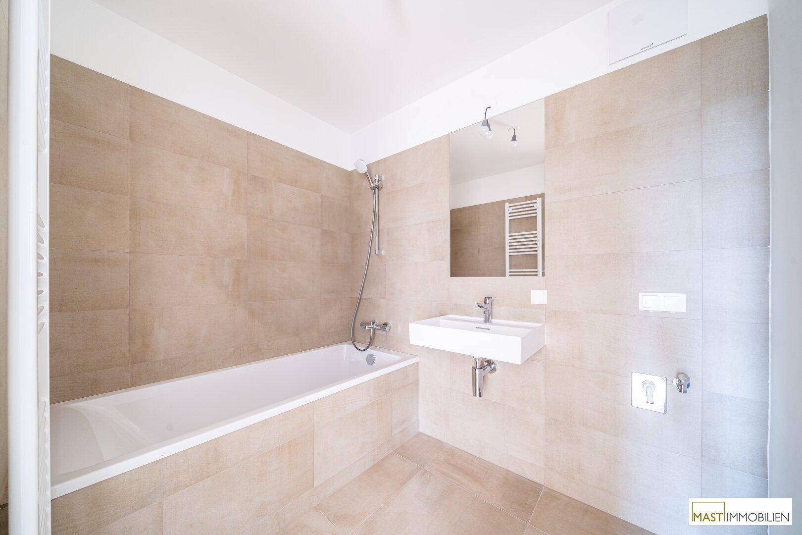 Helles Badezimmer mit Badewanne, modernem Waschbecken und beigefarbenen Wand- und Bodenfliesen.
