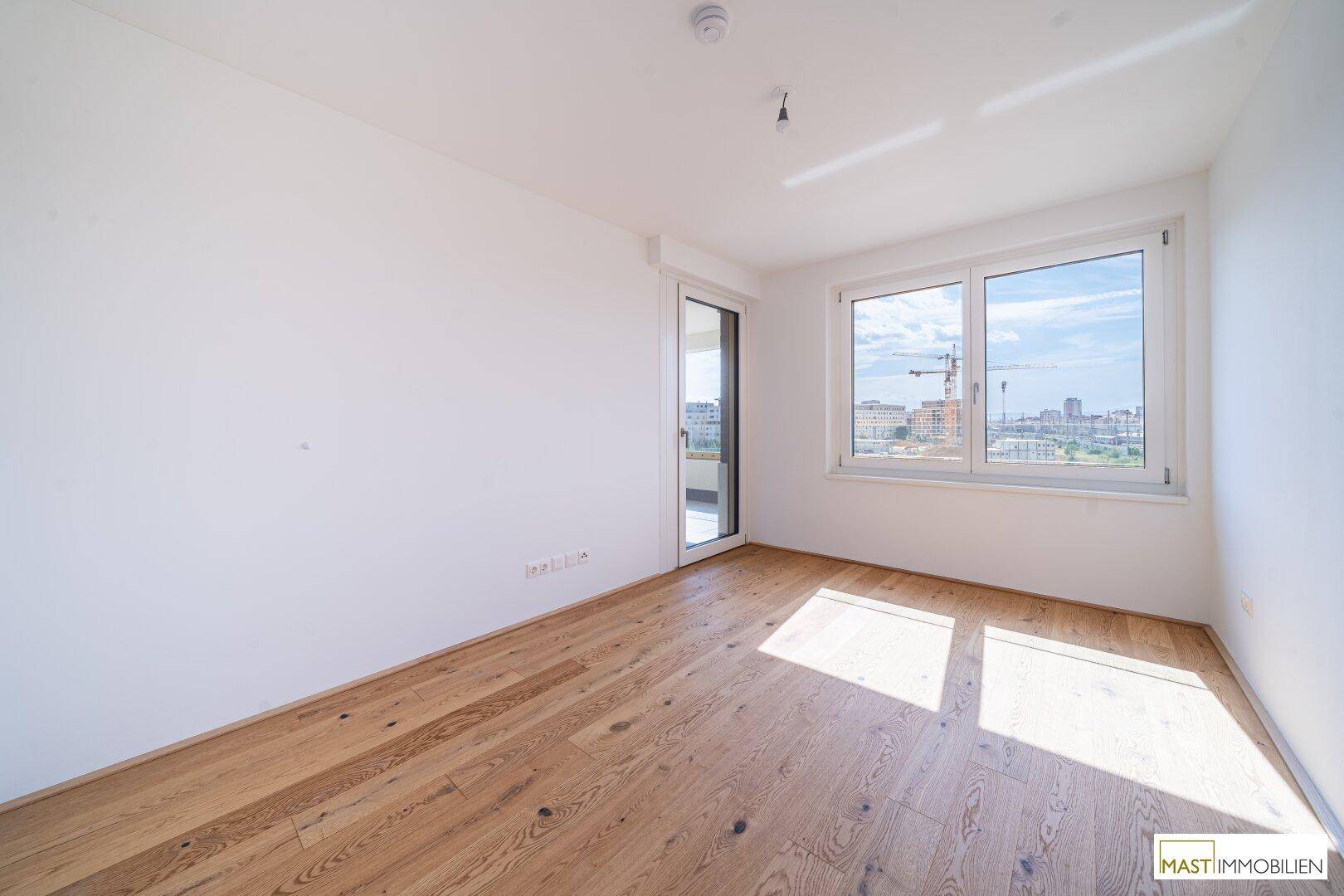 Helles Schlafzimmer mit Parkettboden und großen Fenstern, die viel Tageslicht hereinlassen.