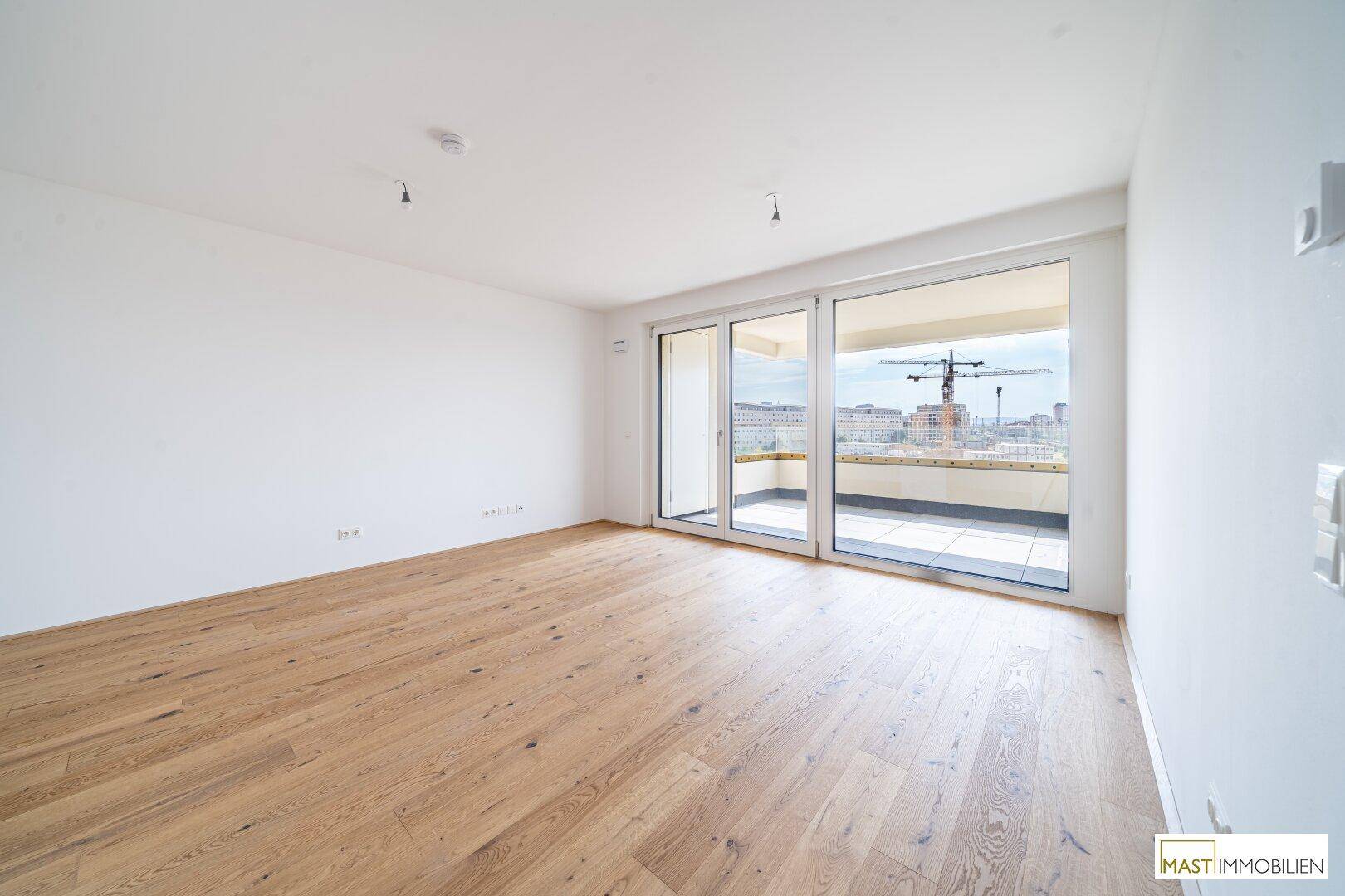 Heller, leerer Wohnraum mit hochwertigem Parkettboden und Zugang zu einer großen Terrasse.