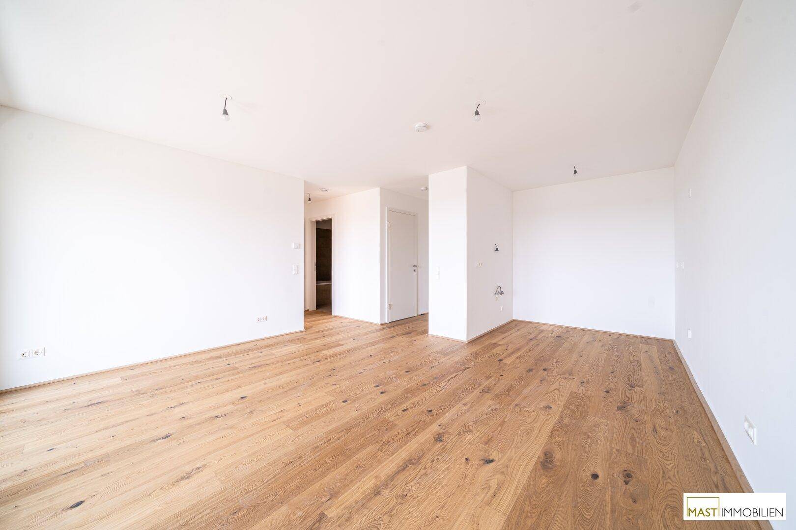 Geräumiger, heller Raum mit Holzparkett und Zugang zu weiteren Zimmern.